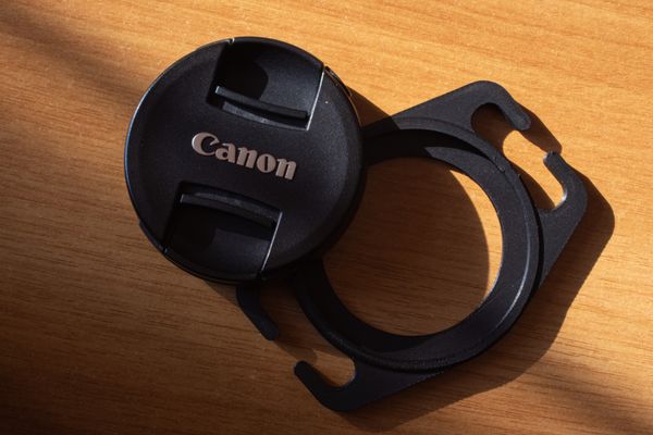 Picture of a Canon lens cap and a black, 3d-printed lens cap holder sitting on a wooden table