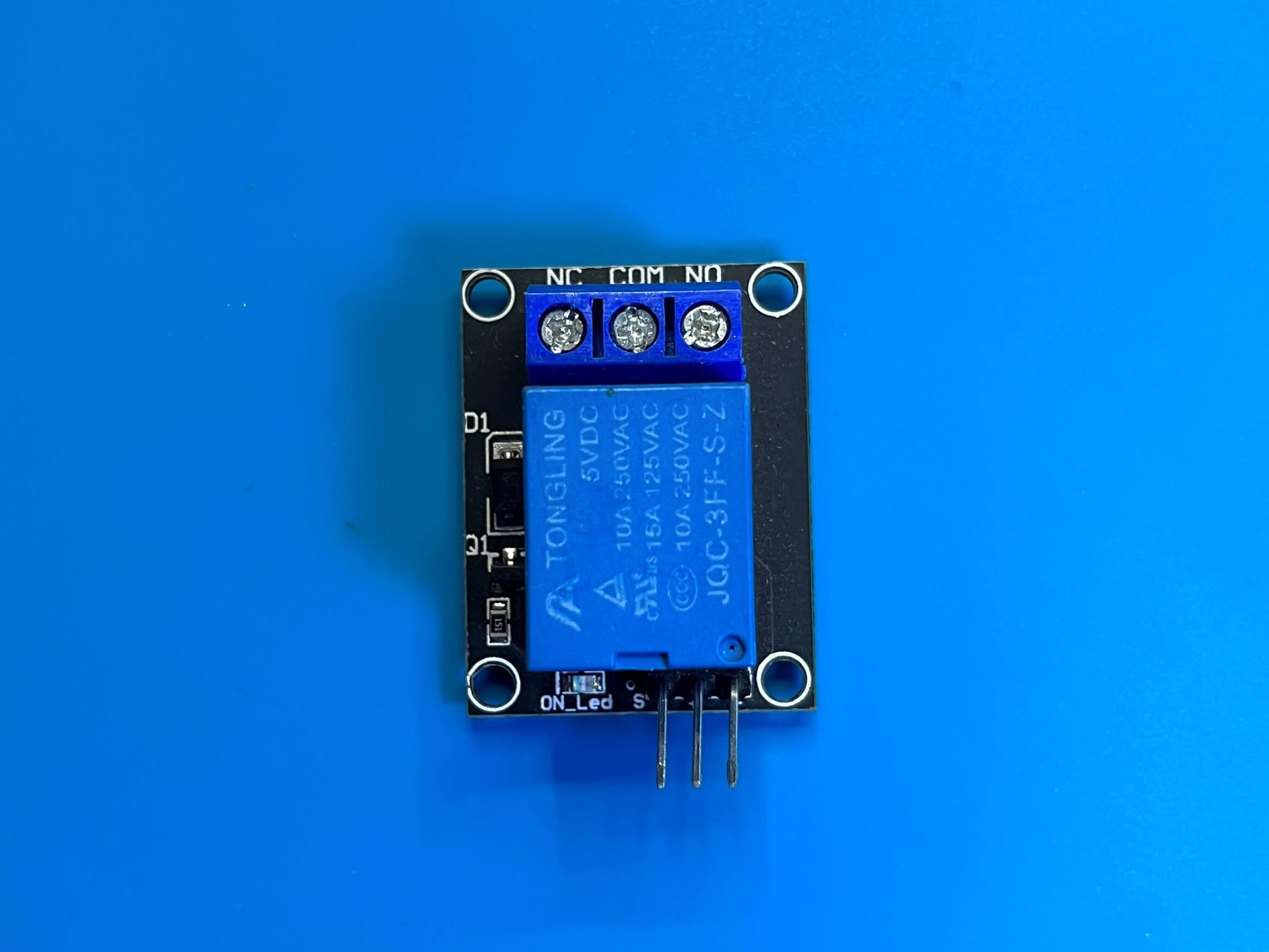 Picture of a low-voltage relay, on a blue electronics soldeting mat