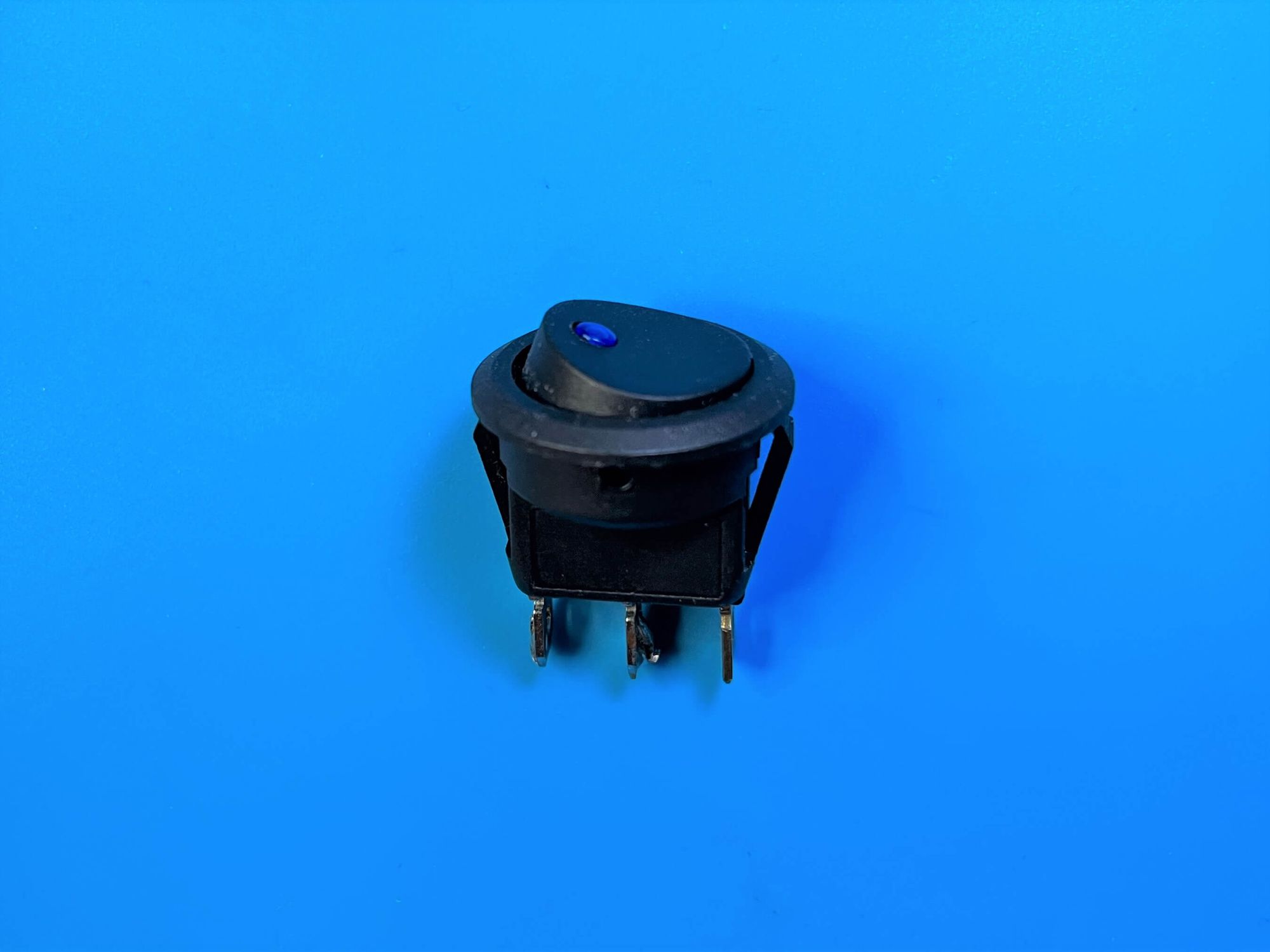 Picture of an automotive toggle switch with three pins and an indicator LED, on a blue electronics mat.