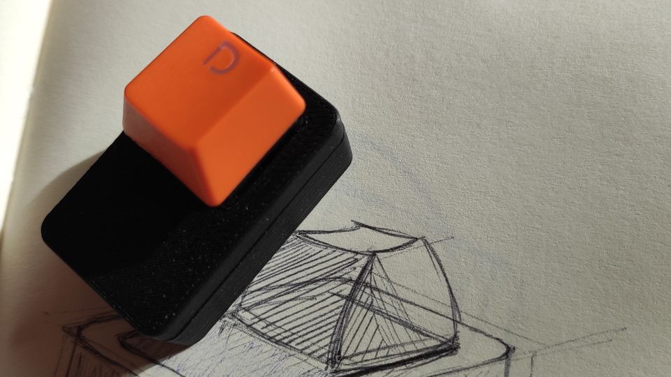 Photo of a 3d printed case with an orange keyboard switch, sitting on a pen sketch of the same design